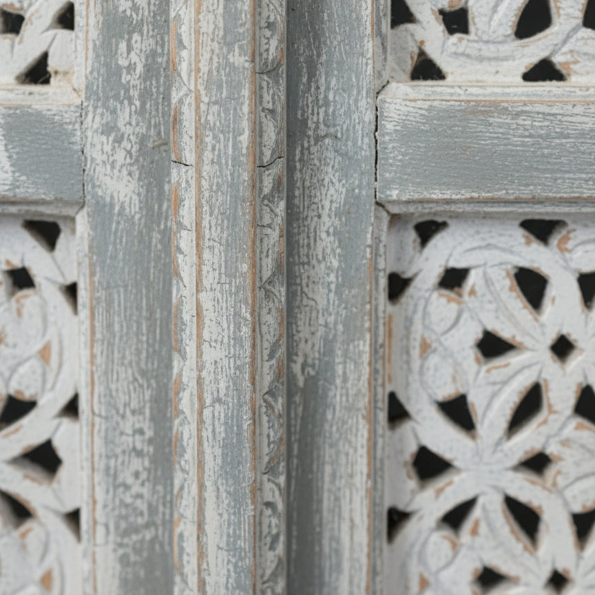 Close-up of carved wood panel with faded gray paint, ornate floral tribal patterns