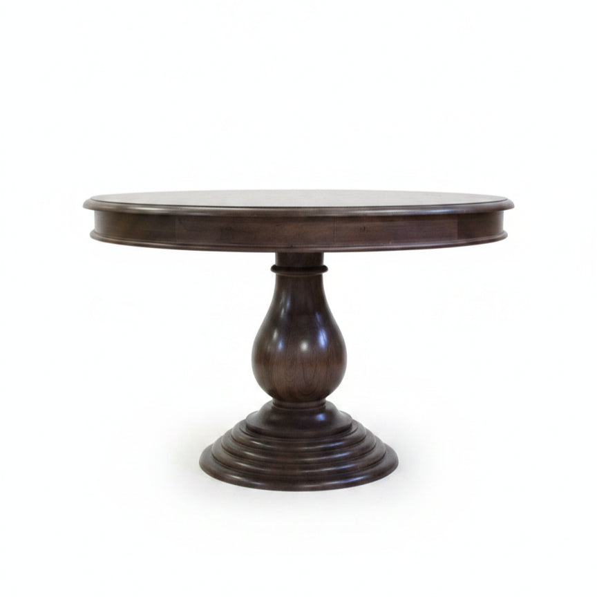 Elegant round wooden dining table with a polished dark finish, featuring a sturdy carved pedestal base, reflecting handcrafted tribal decor artistry.