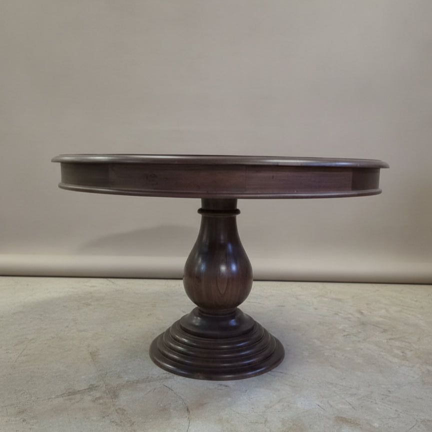 Round wooden dining table with a sturdy carved pedestal base, showcasing handcrafted tribal decor and elegant solid wood finish.