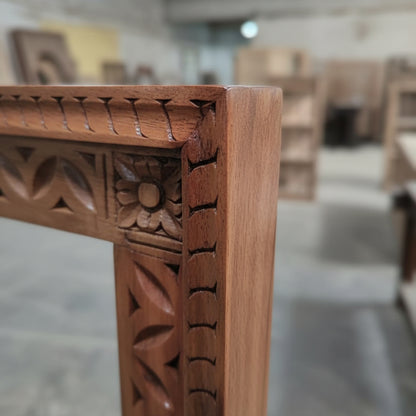 Hand-carved wooden frame with floral tribal motifs in a workshop setting