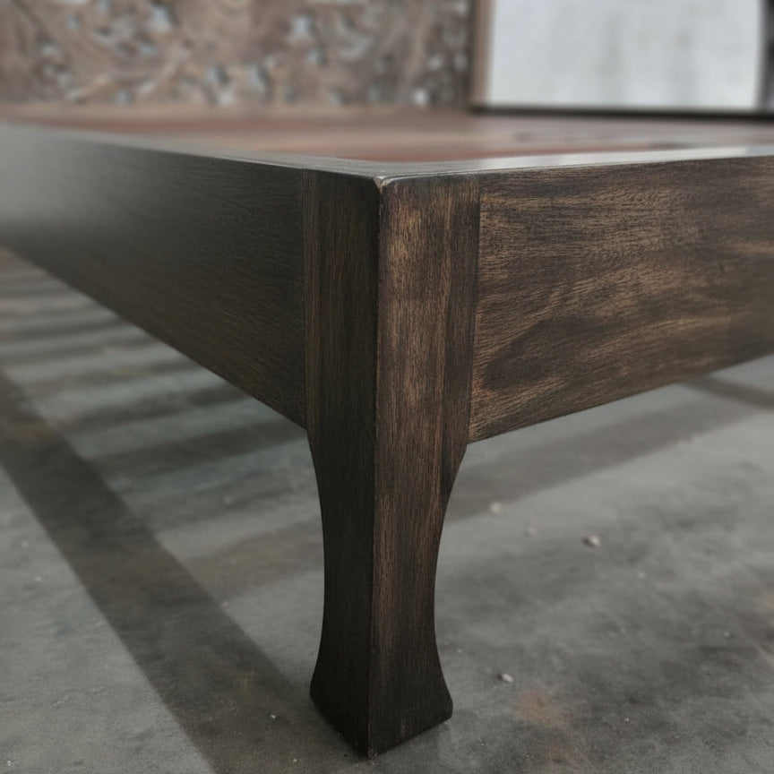 Handcrafted wooden bed frame with dark finish and carved leg detail on stone floor
