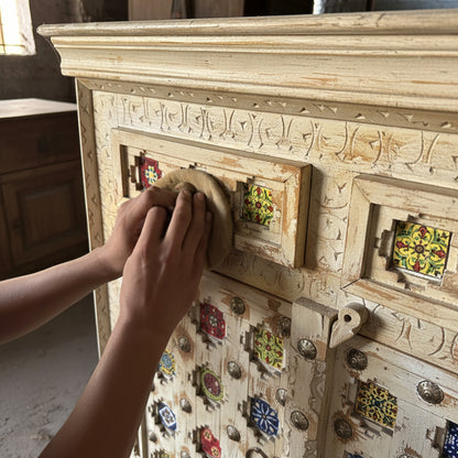 Hand polishing carved wooden tribal handicraft cabinet with colorful tile accents