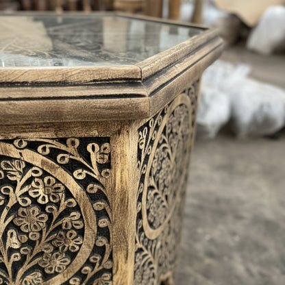 Handcrafted wooden table with intricate tribal floral carvings and glass top