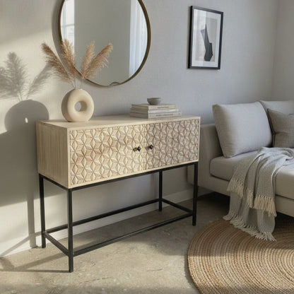 Wooden cabinet with intricate carved tribal patterns, placed in a modern living room setting with a round mirror, minimalist decor, and soft natural light.