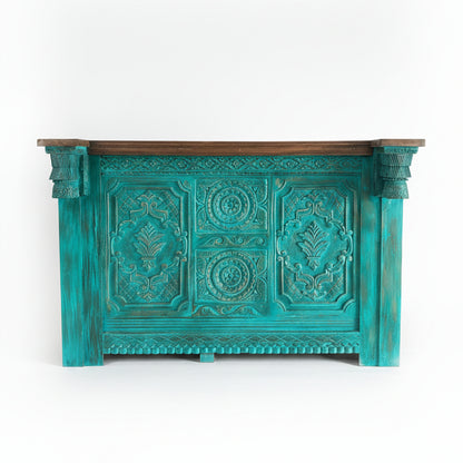 Handcrafted wooden service counter in turquoise with intricate tribal carvings and a contrasting dark wood top, showcasing unique decor and artisanal quality.