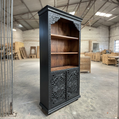 Handcrafted wooden bookshelf with ornate carved doors in rustic warehouse setting