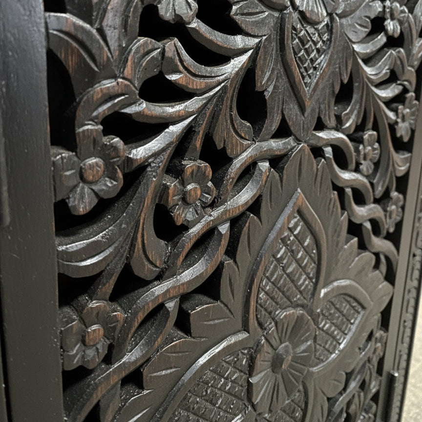 Close-up of dark wood panel with intricate floral hand-carved tribal patterns