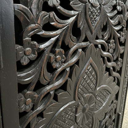 Close-up of dark wood panel with intricate floral hand-carved tribal patterns
