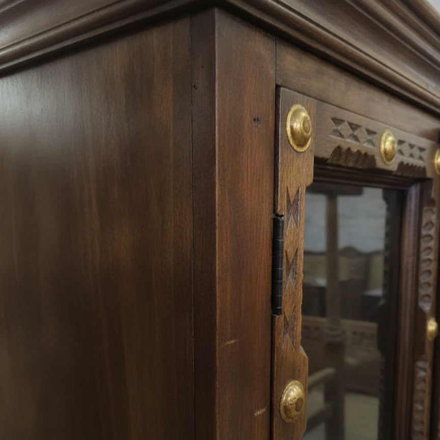 Close-up of finely crafted solid wooden display cabinet corner featuring tribal-style carved details and brass decorative accents on the door frame.